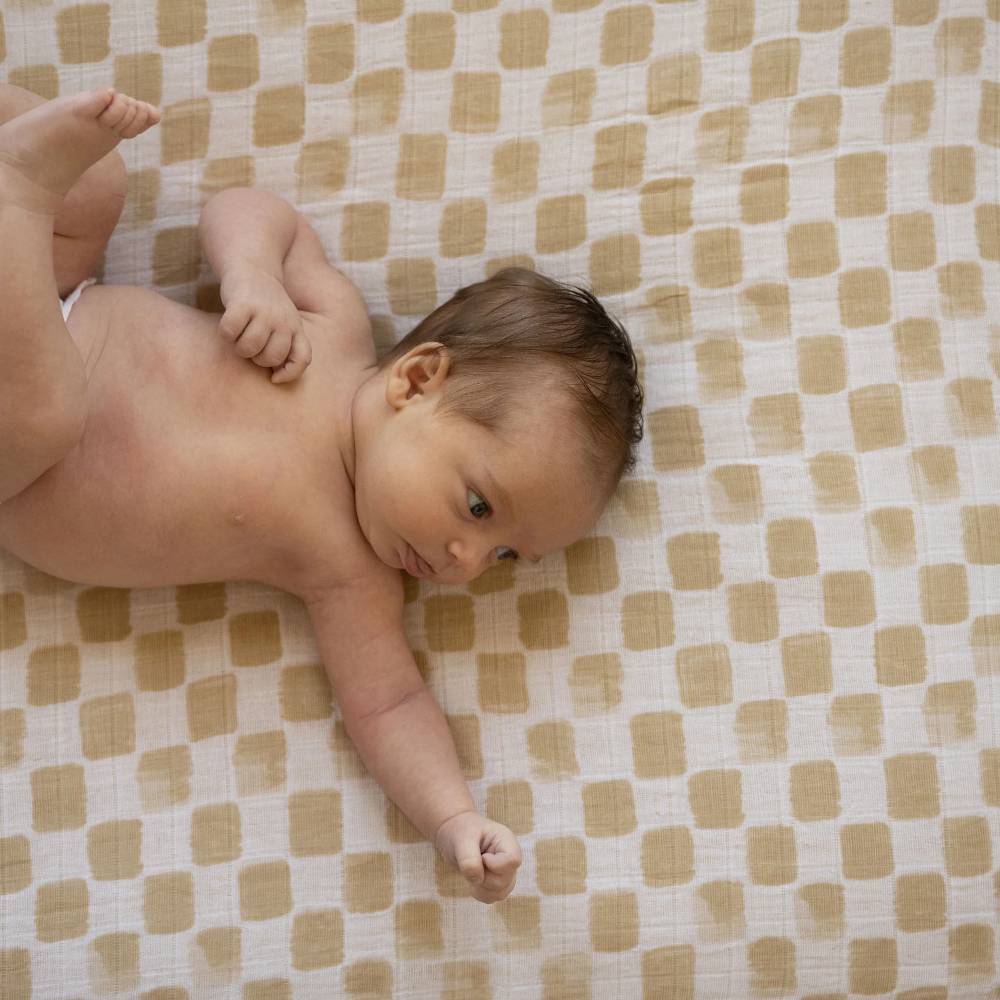 Baby lying on a beige and white checkered muslin blanket