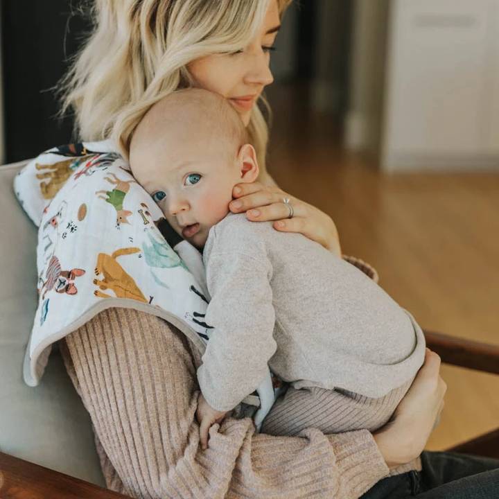 Woman holding a baby with a dog themed white cotton muslin burp cloth on her shoulder.