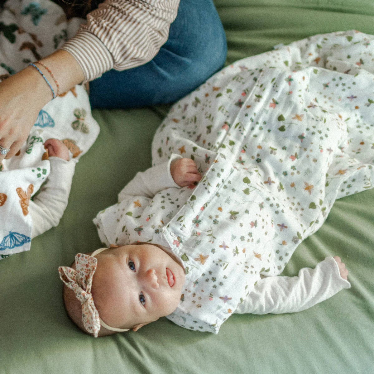 Baby in a floral sleeping bag lying on a green surface.