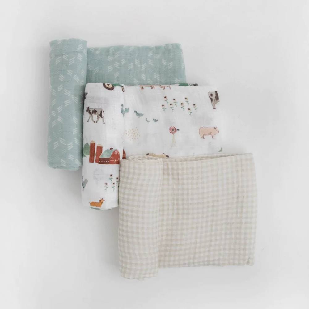Three cotton muslin swaddles with blue and white line print, farmyard theme and tan gingham pattern on a white background 