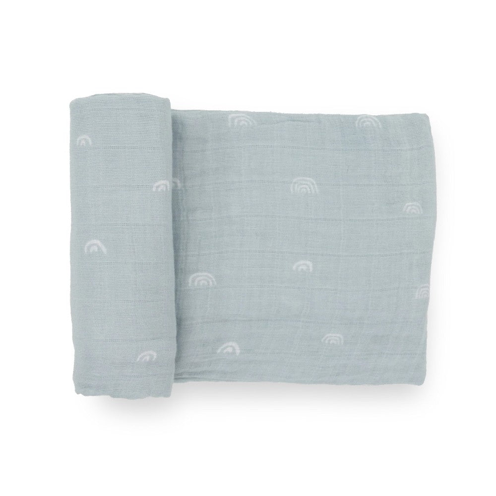 A light blue cotton muslin swaddle blanket with white rainbow patterns on a white background