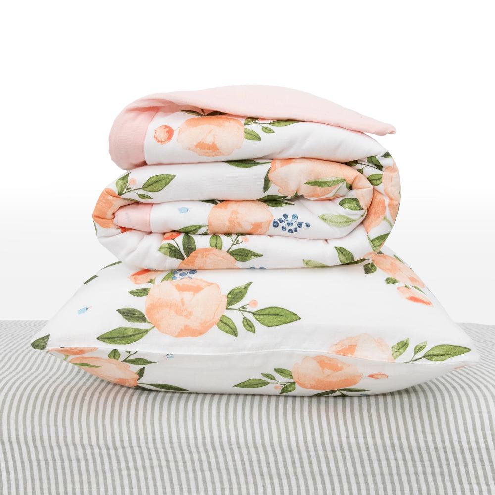 White Stackincluding baby blanket and pillow with watercolour rose patterns on a white background and grey striped sheet. 