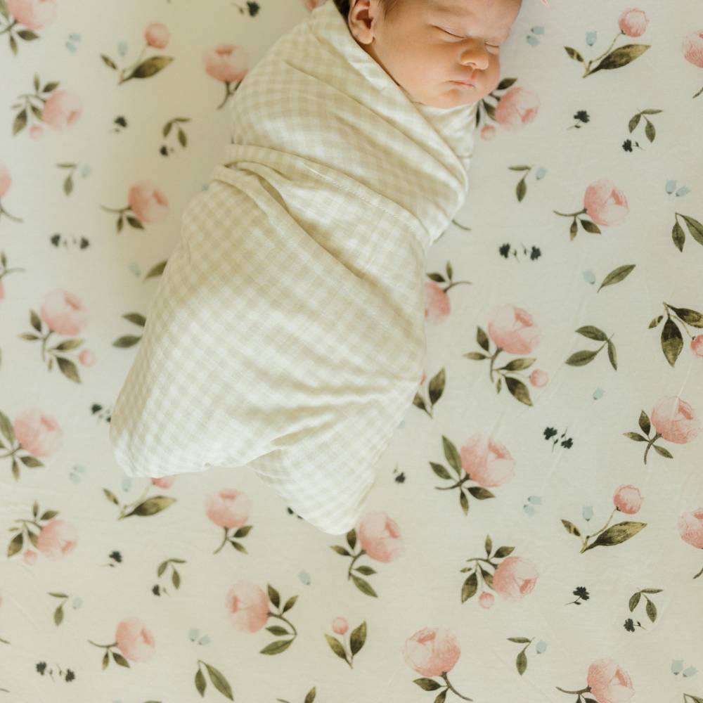 Newborn baby swaddled in white and beige check blanket on floral-patterned blanket