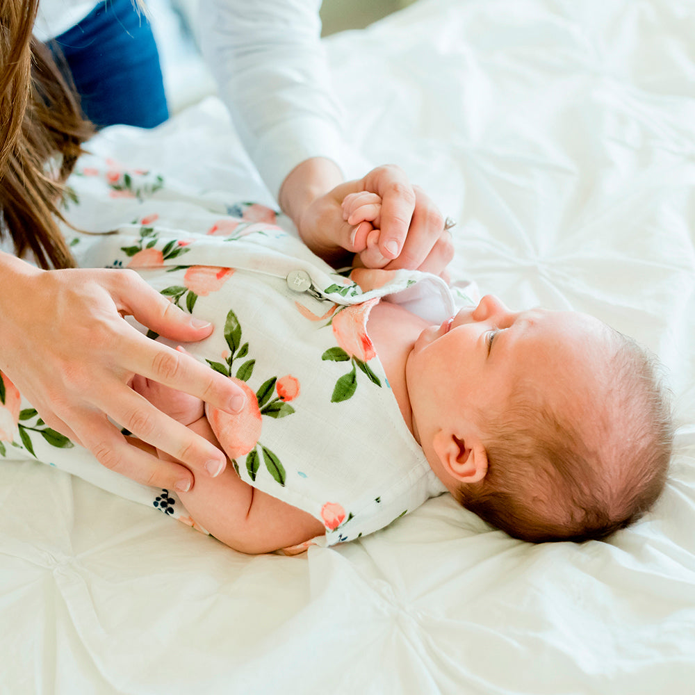 Baby in a floral sleeping bag being held by an adult on a white blanket