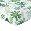 Little unicorn cotton muslin changing pad cover in a white and green tropical leaf pattern on a bed with white background