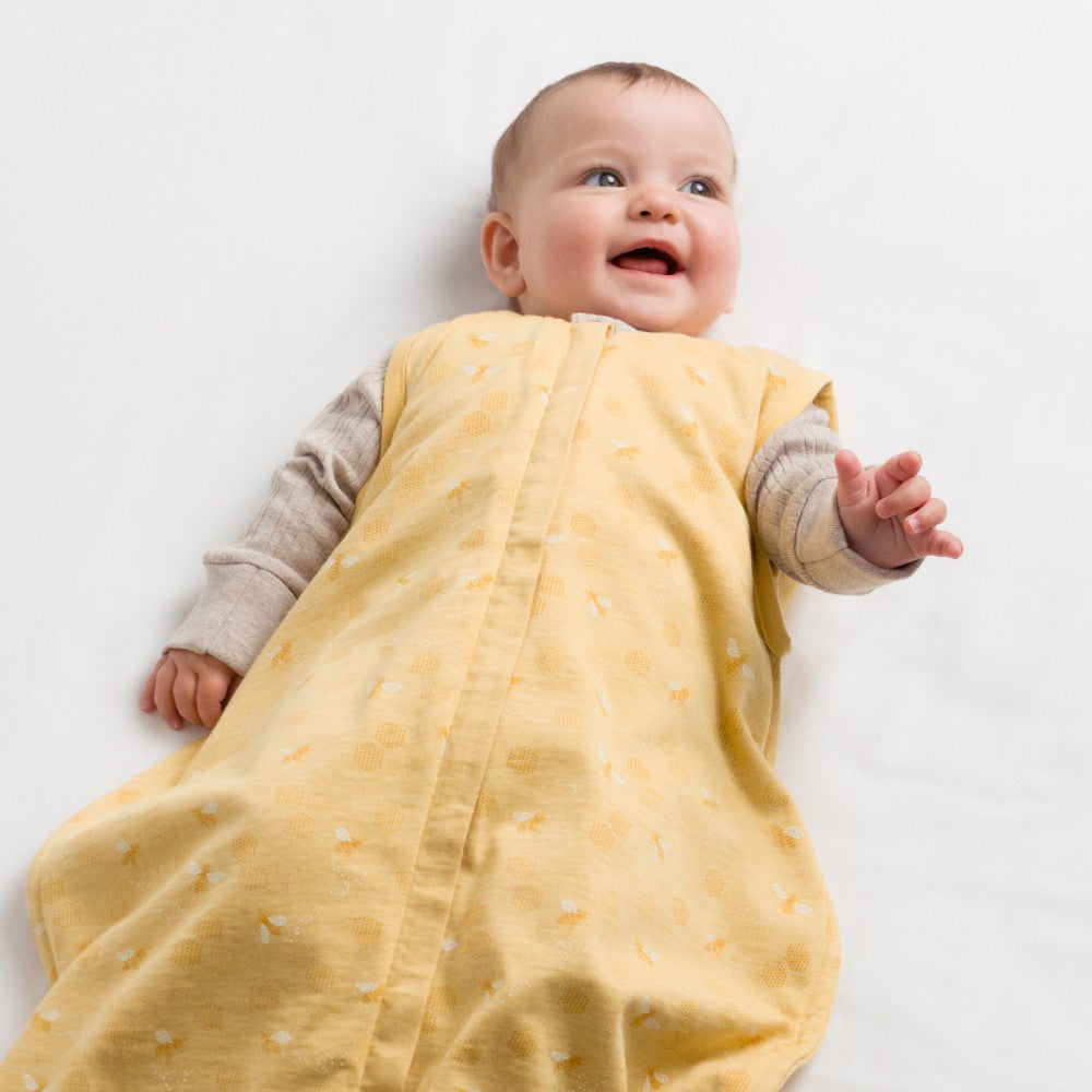 Baby wearing a yellow woolbabe sleeping bag with a white background