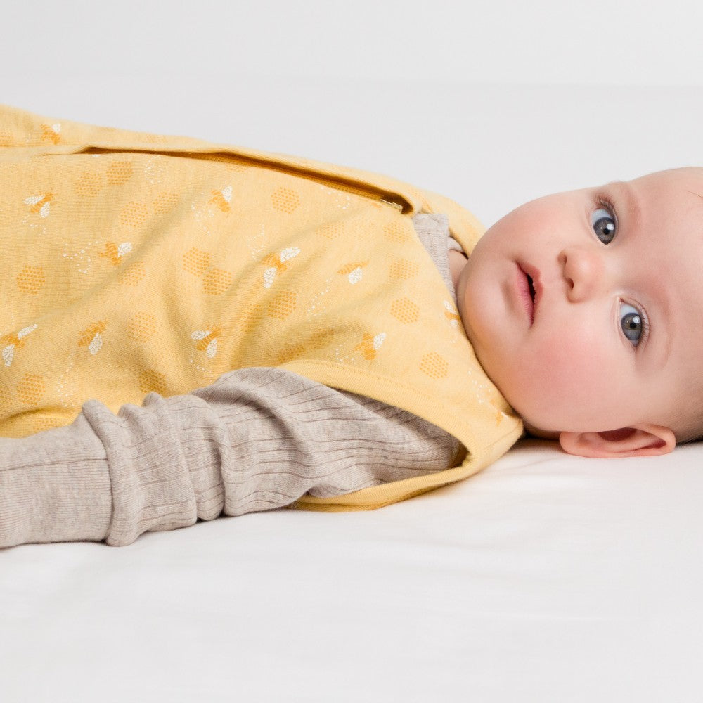Baby wearing a yellow and gray baby sleeping bag with bee print on a white background