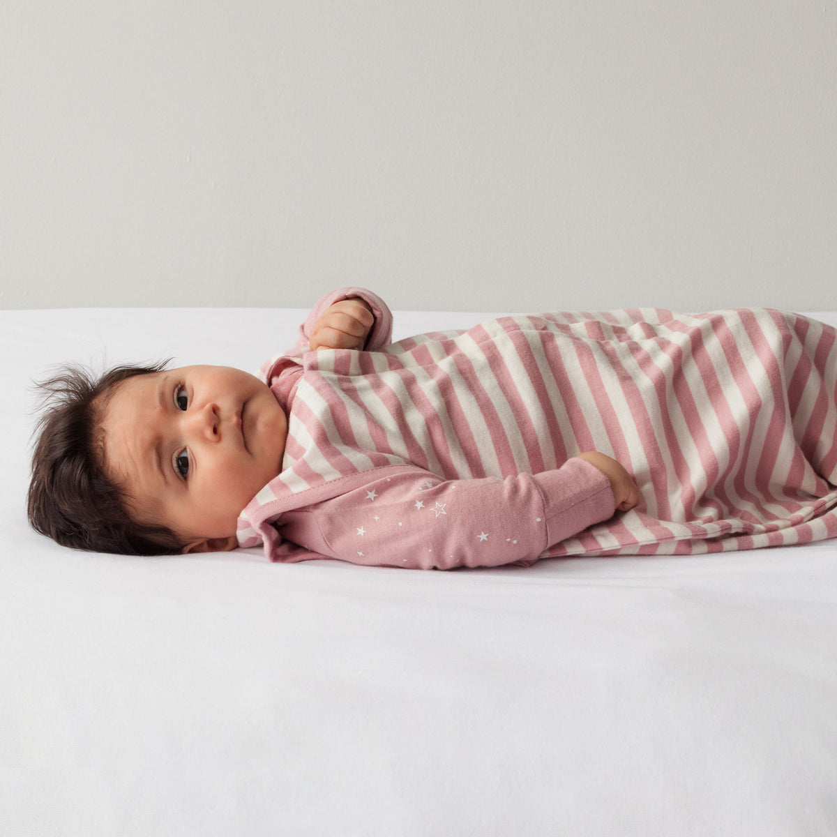 Baby wrapped in a pink and white striped sleeping sack on a white surface