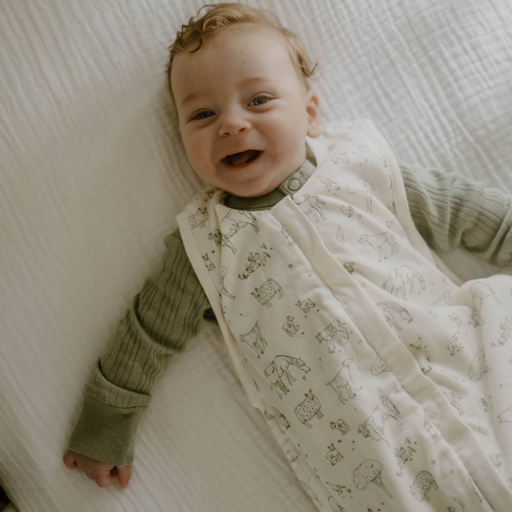 Baby wearing a Farmyard design 3 seasons sleeping bag lying down smiling. 