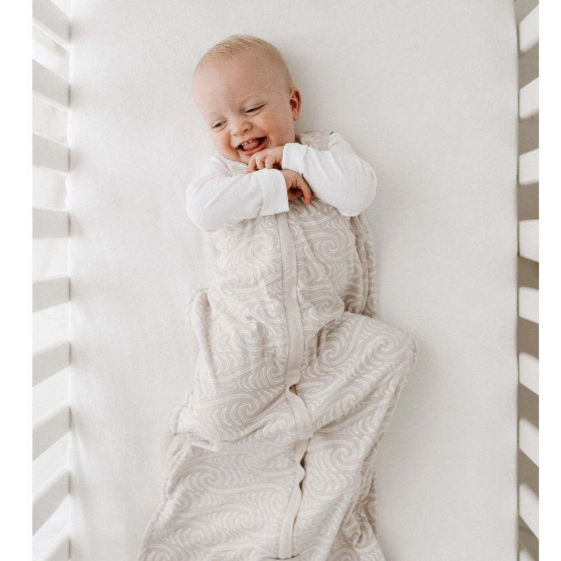 Baby lying in a crib with a maori patterned beige sleep sack