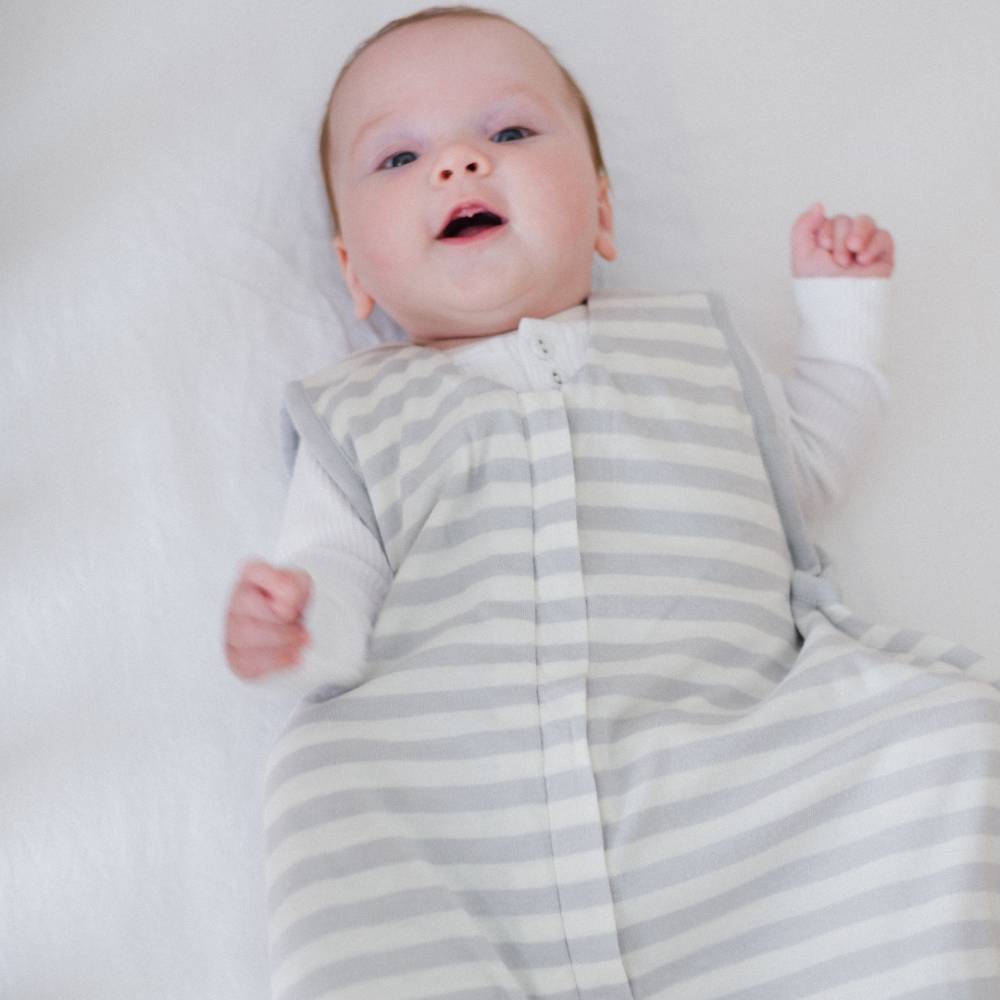 Baby wearing a gray and white striped sleep bag on a plain background