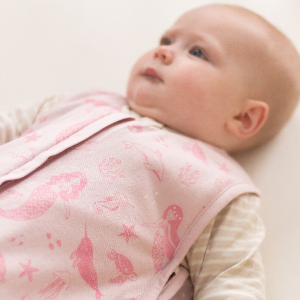 Baby wearing a pink patterned sleep sack on a white background