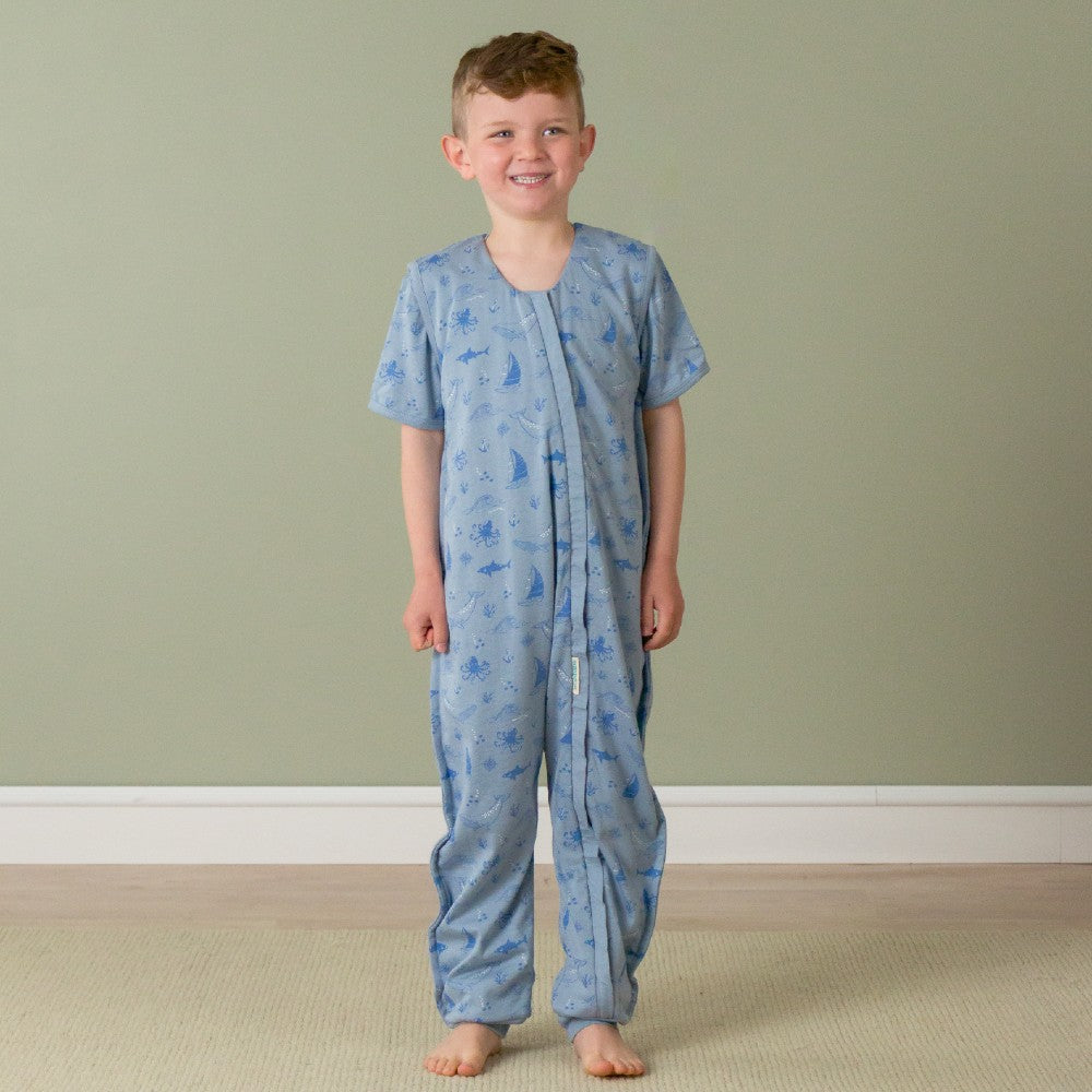 Child wearing a sleepsuit with animal patterns against a plain wall.