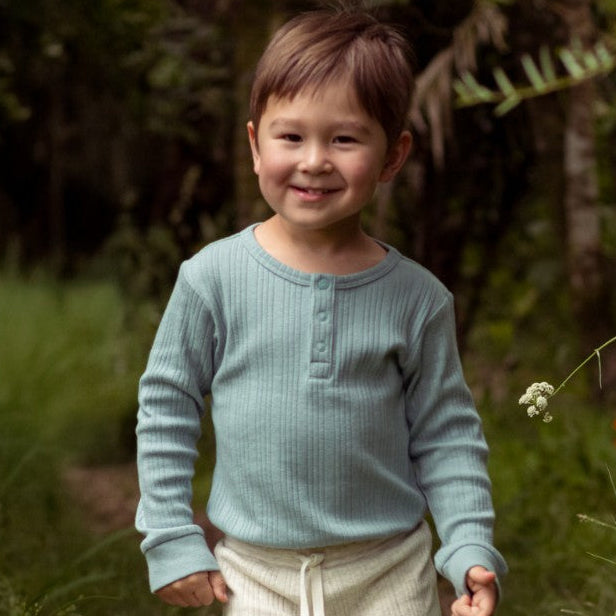 Child wearing ribbed long sleeve baby bodysuit standing in a grassy outdoor setting.
