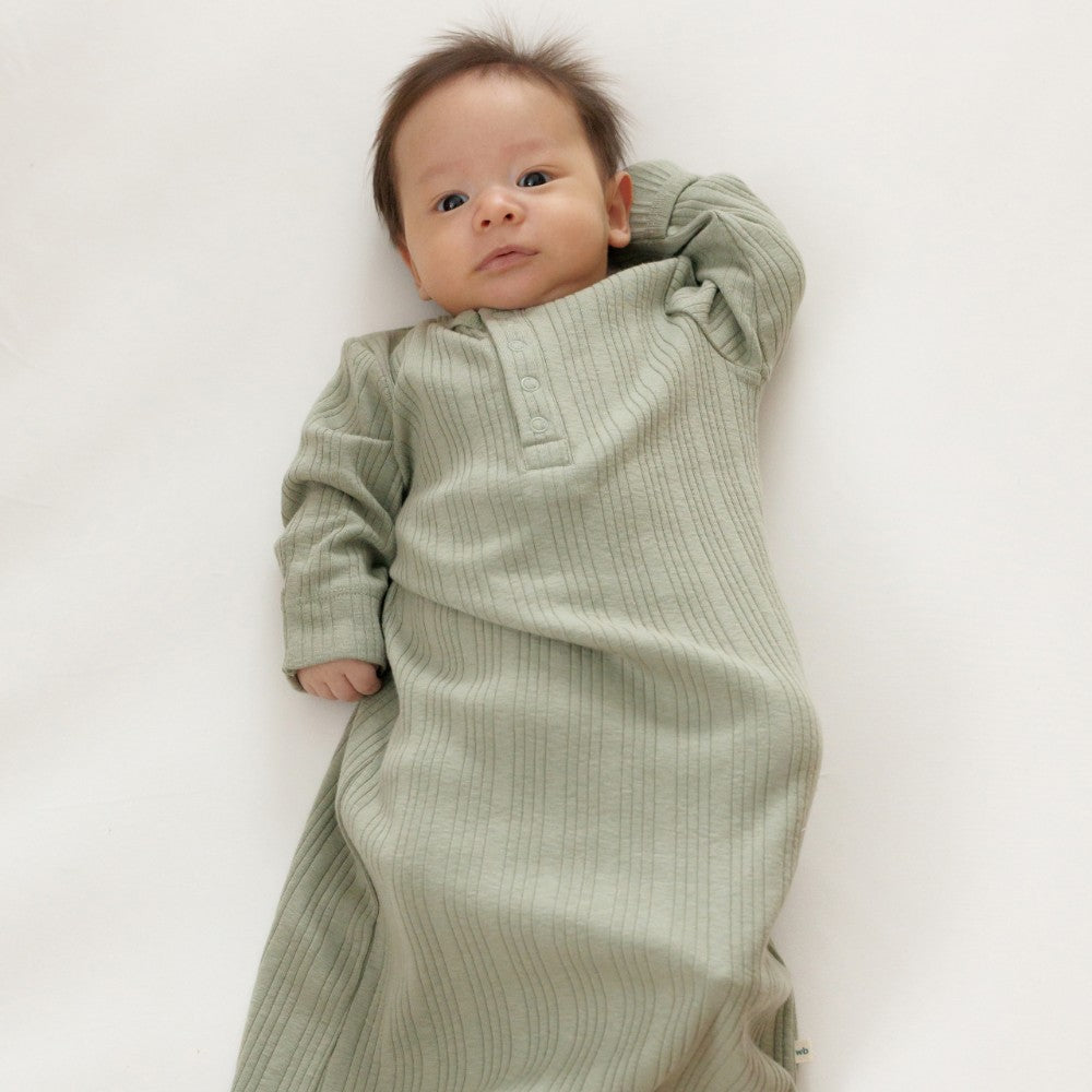 Baby dressed in a green rib woolbabe baby nightie on a white background