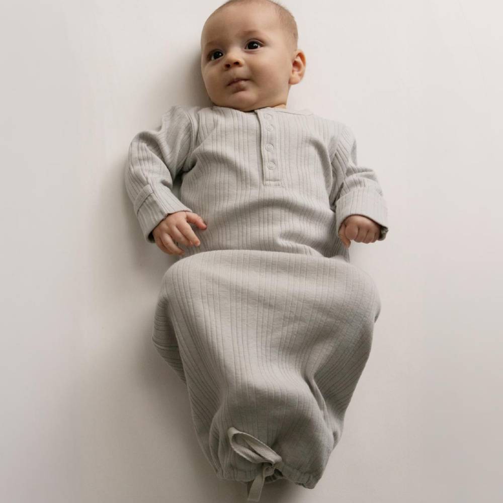 Baby lying down wearing a Woolbabe Pebble Marl gown. 