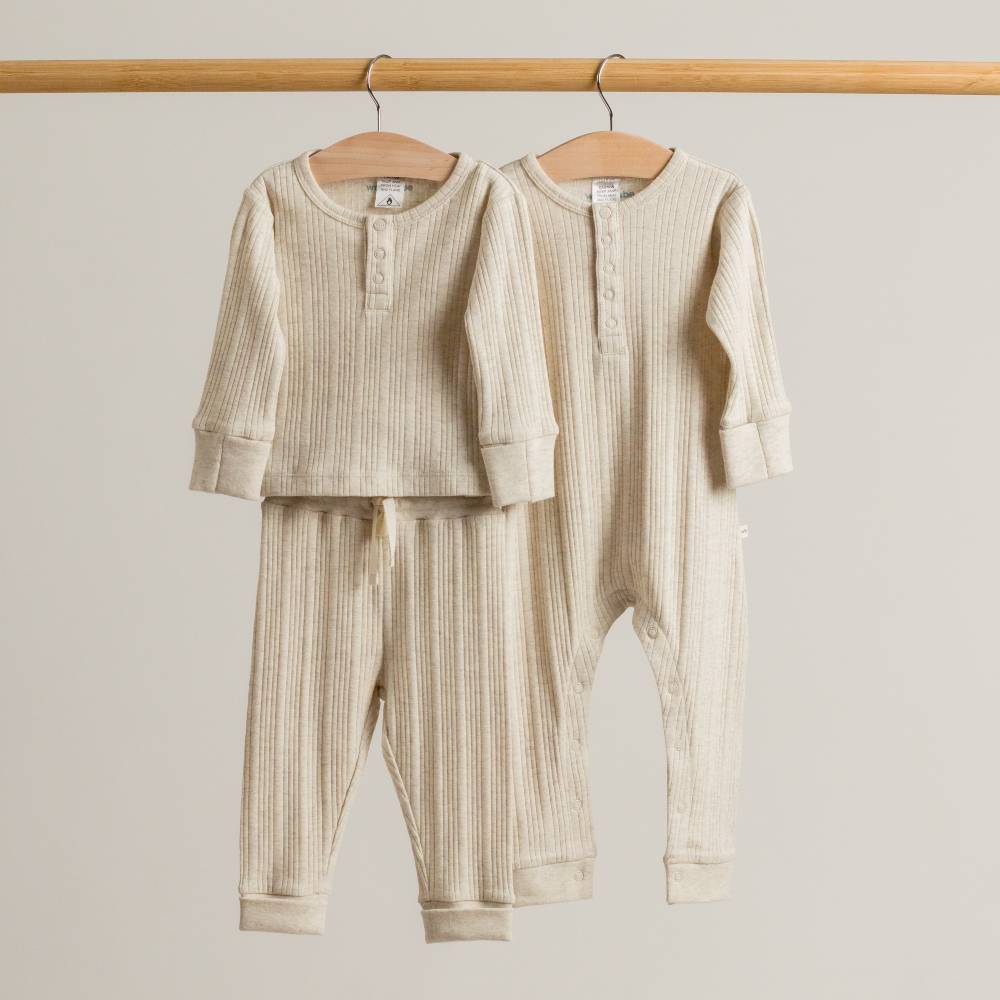woolbabe merino rib baby outfits hanging on a wooden rod against a plain background