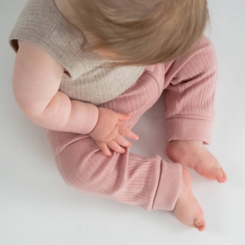 Baby wearing pink ribbed pants and a beige top on a white background