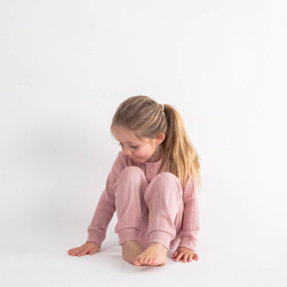 Young girl in pink rib woolbabe pajamas sitting on a white surface