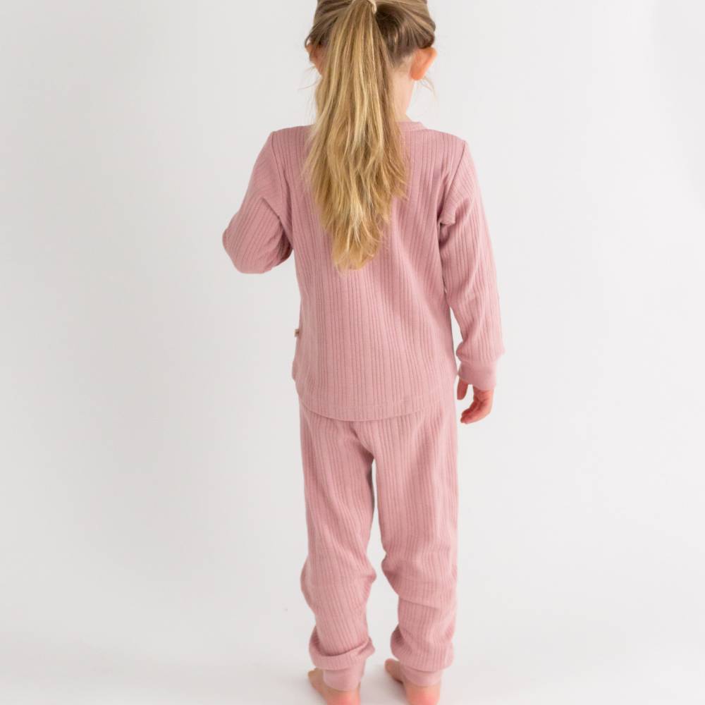 Child wearing pink ribbed pajamas on a white background