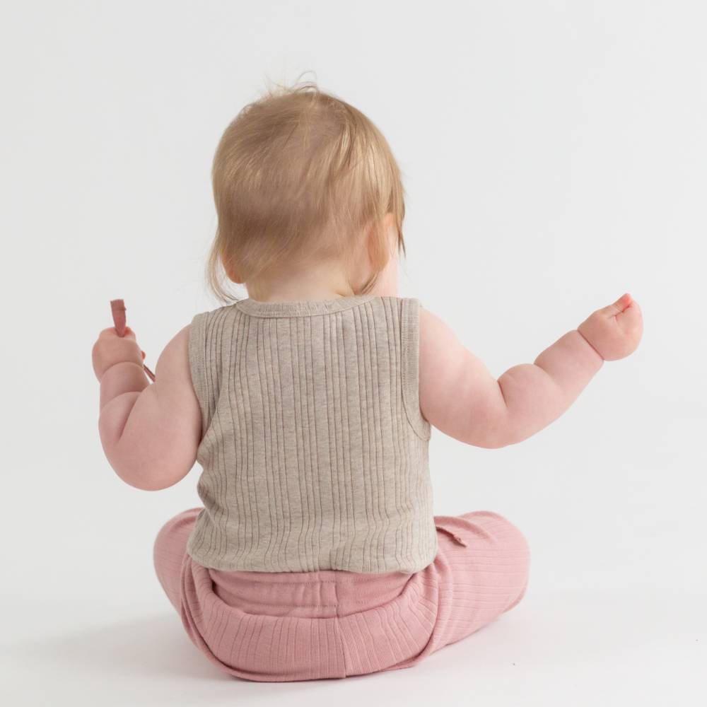 Baby wearing a beige ribbed vest and pink pants on a white background
