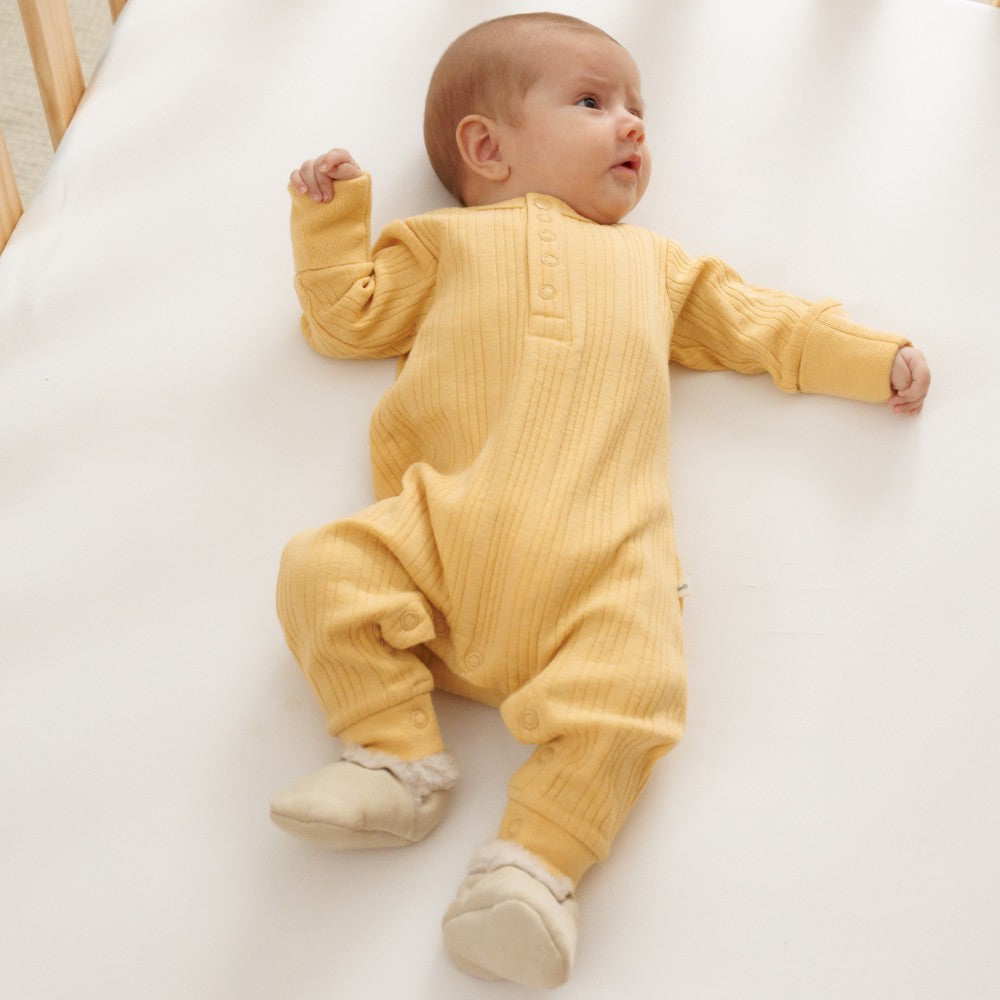 Baby in a yellow woolbabe merino stretch n grow outfit lying on a white surface