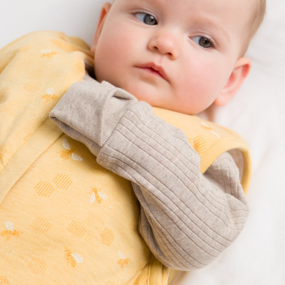 Baby wrapped in a yellow blanket with a neutral-colored wrap, on a white background