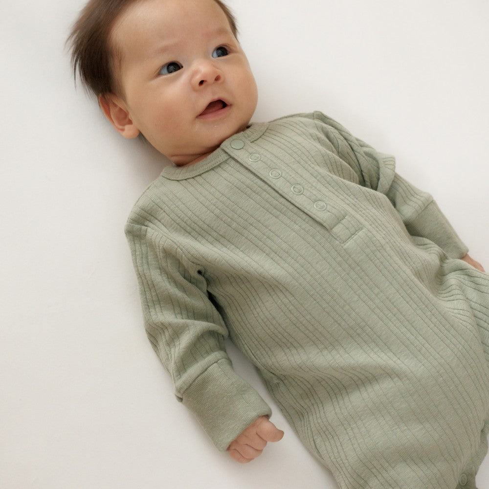 Baby wearing a green ribbed onesie on a white background