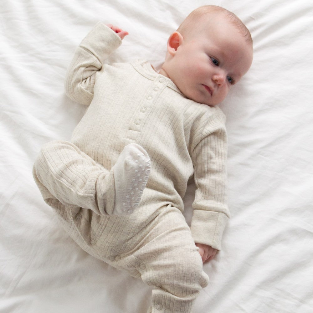 Baby wearing a cream merino suit with crotch snaps lying on a white surface