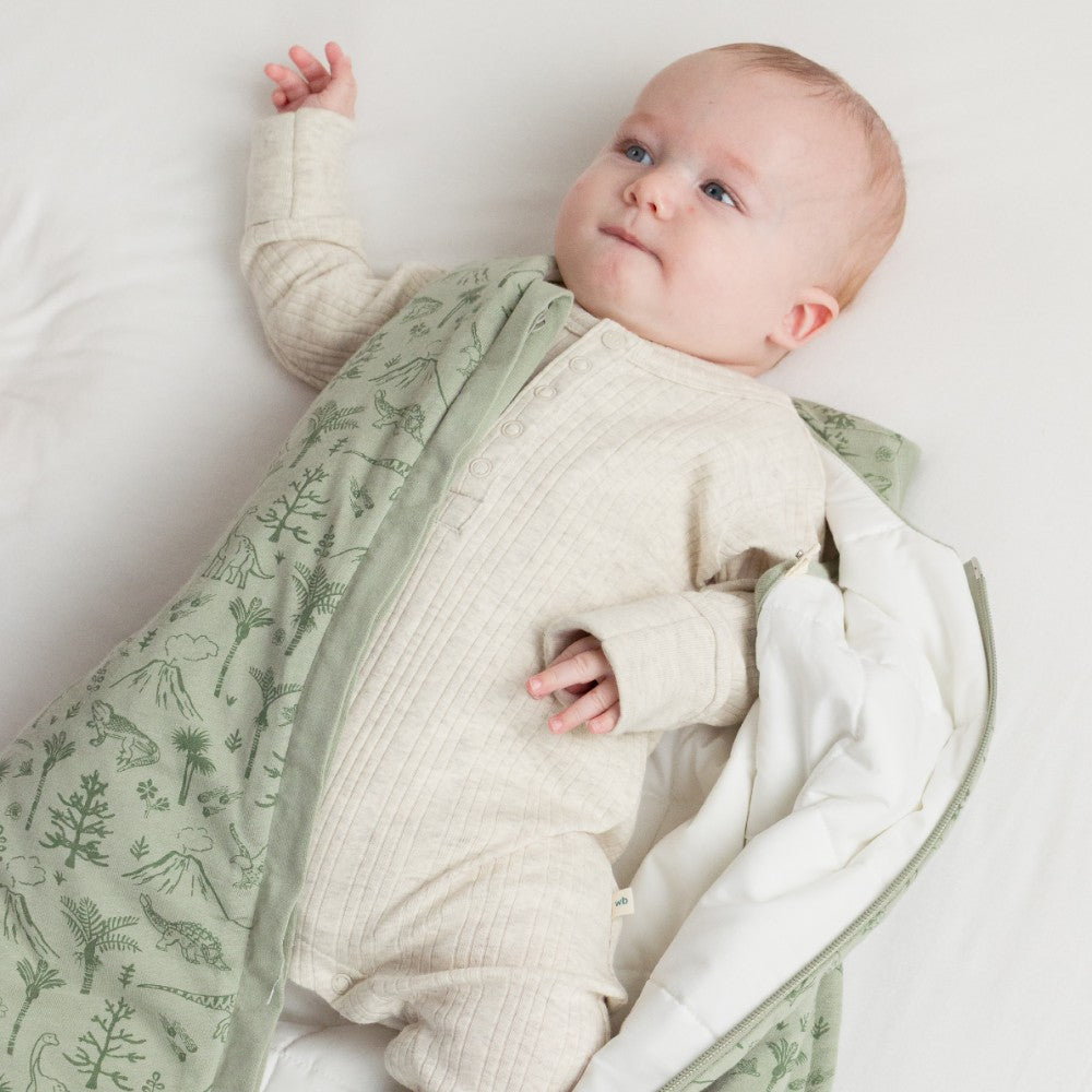Baby wrapped in a green and white sleeping bag wearing a cream merino onesie on a white background