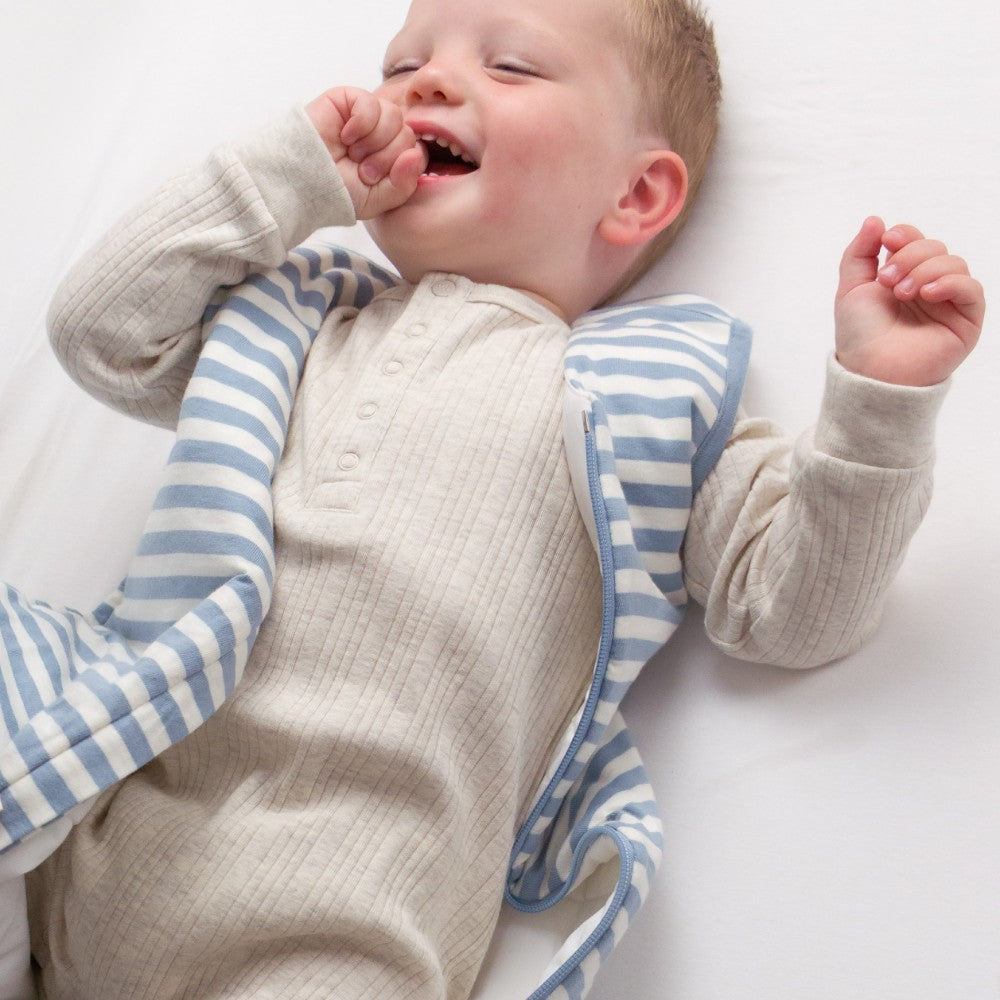 Baby wearing a beige outfit with blue and white striped sleeves and legs on a white background