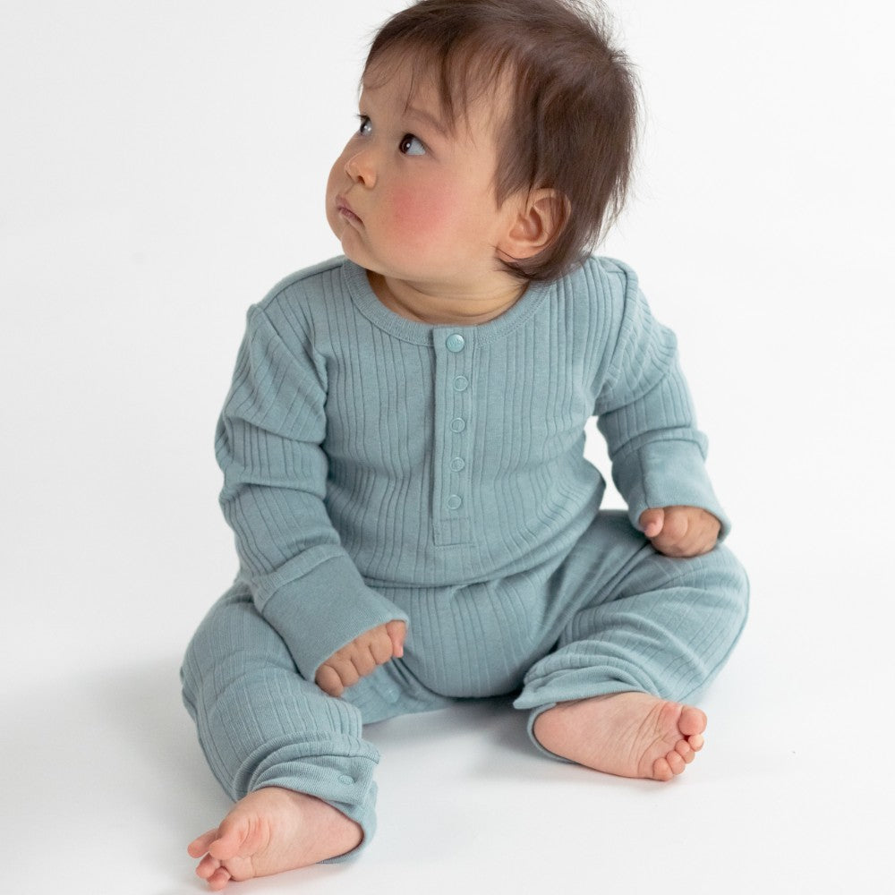 Baby wearing a light blue ribbed merino onesie sitting on a white background