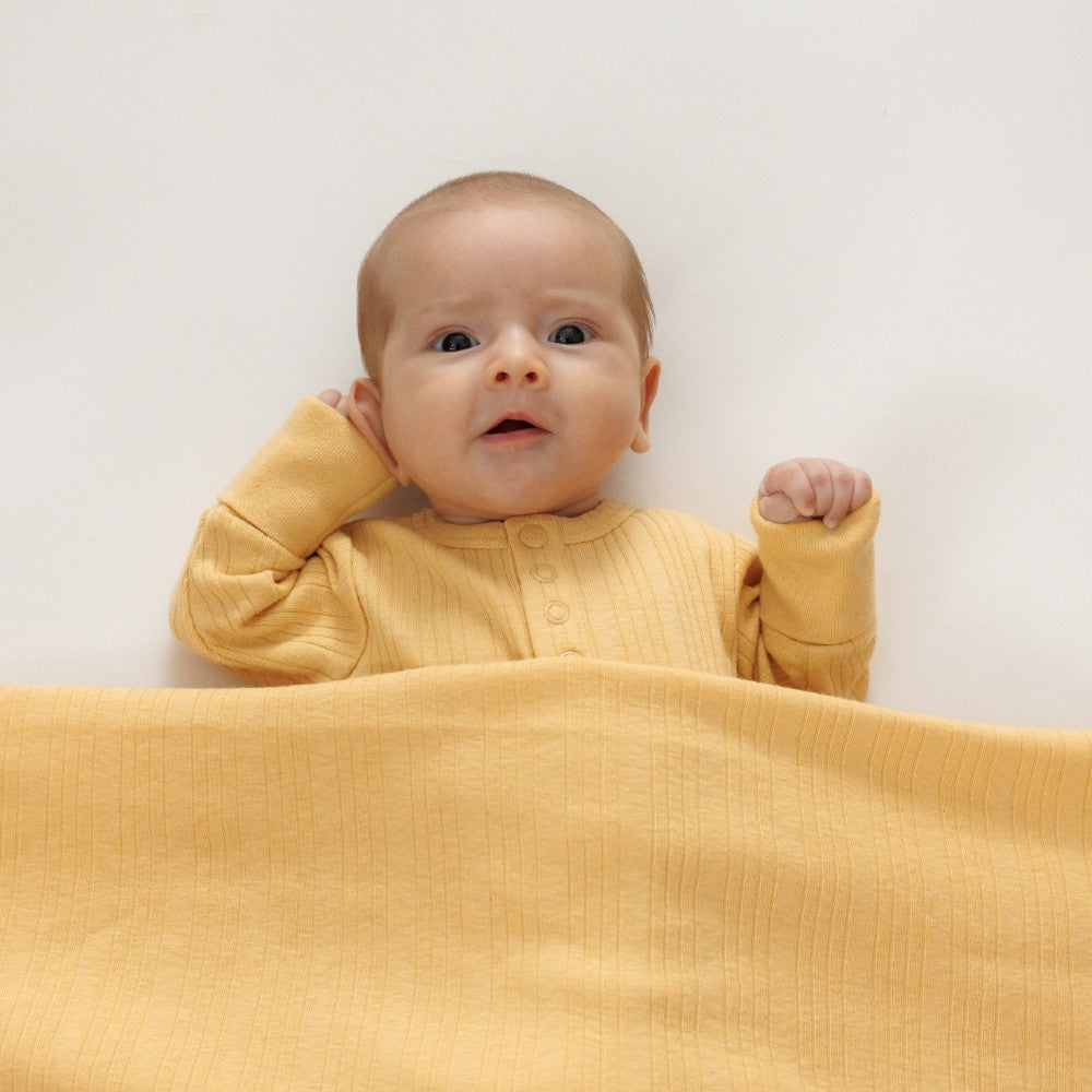 Baby in a yellow outfit lying on a yellow blanket against a white background