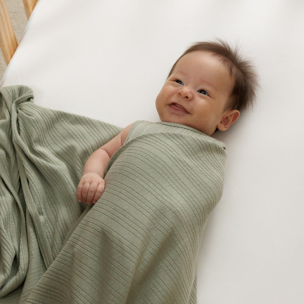 Baby wrapped in a green woolbabe swaddle blanket on a white background