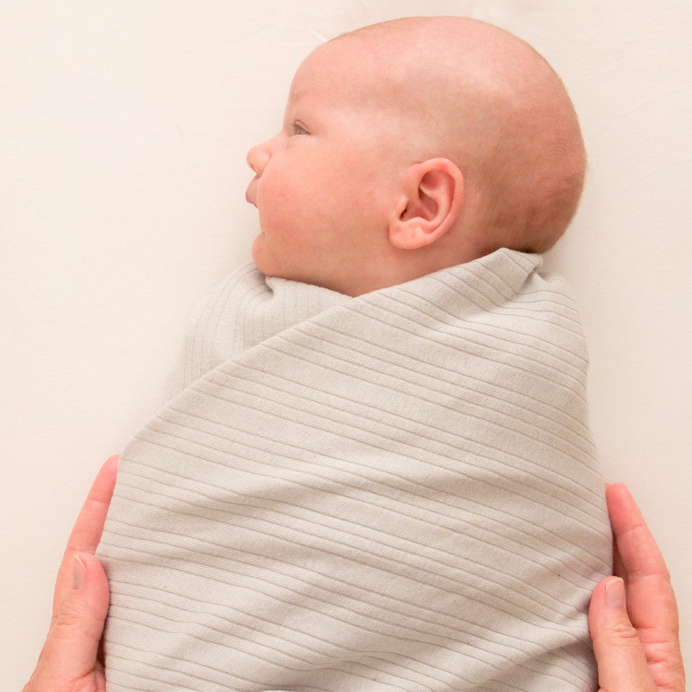 Baby wrapped in a light gray woolbabe merino swaddle blanket with a neutral background