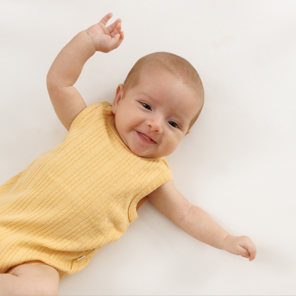 Baby wearing a yellow woolbabe sleeveless romper on a white background