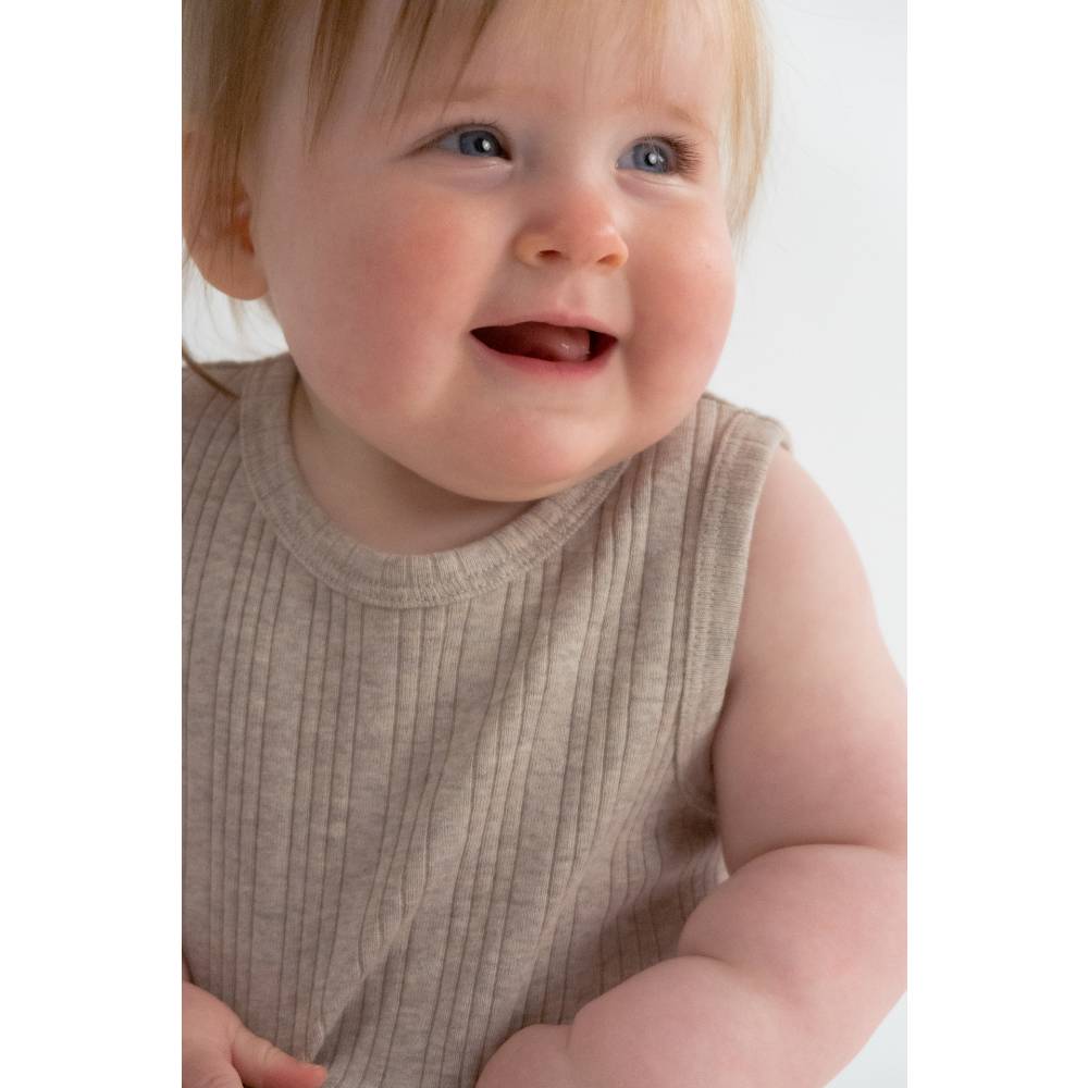 Baby wearing a beige sleeveless shirt against a white background