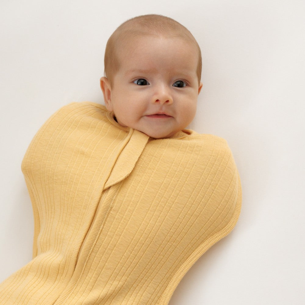 Baby wrapped in a yellow woolbabe zip swaddle on a plain background