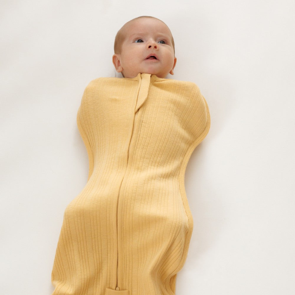 Baby wrapped in a yellow woolbabe zip swaddle on a plain background