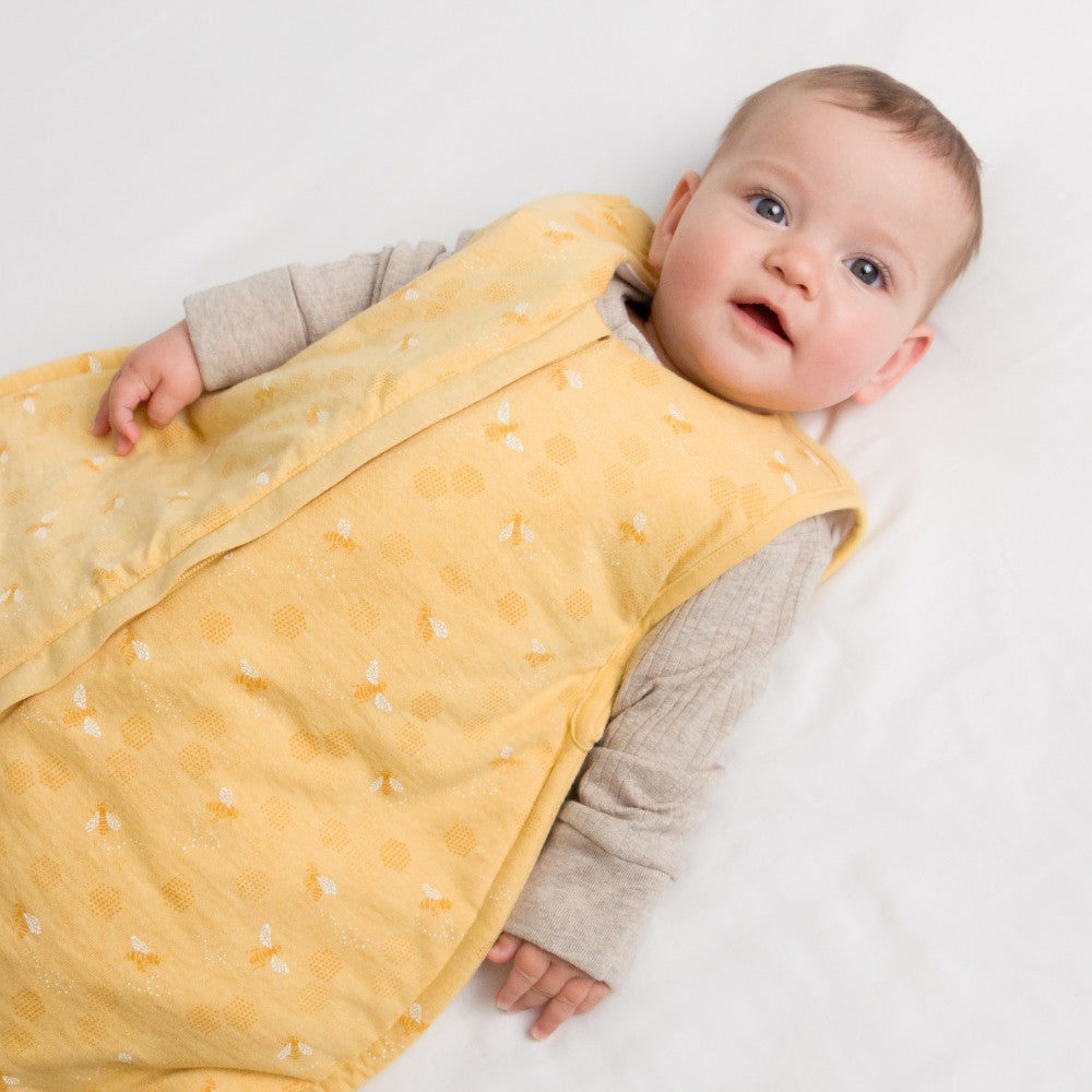 Baby wrapped in a yellow bee print sleeping bag on a white background