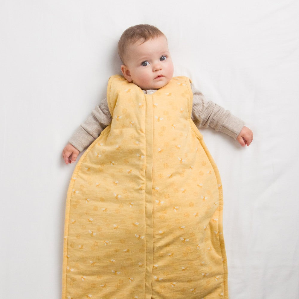 Baby lying on a white surface wearing a yellow sleeping bag
