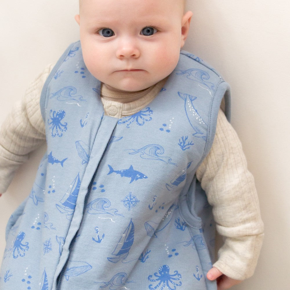 Baby wearing a blue sea-patterned vest against a neutral background