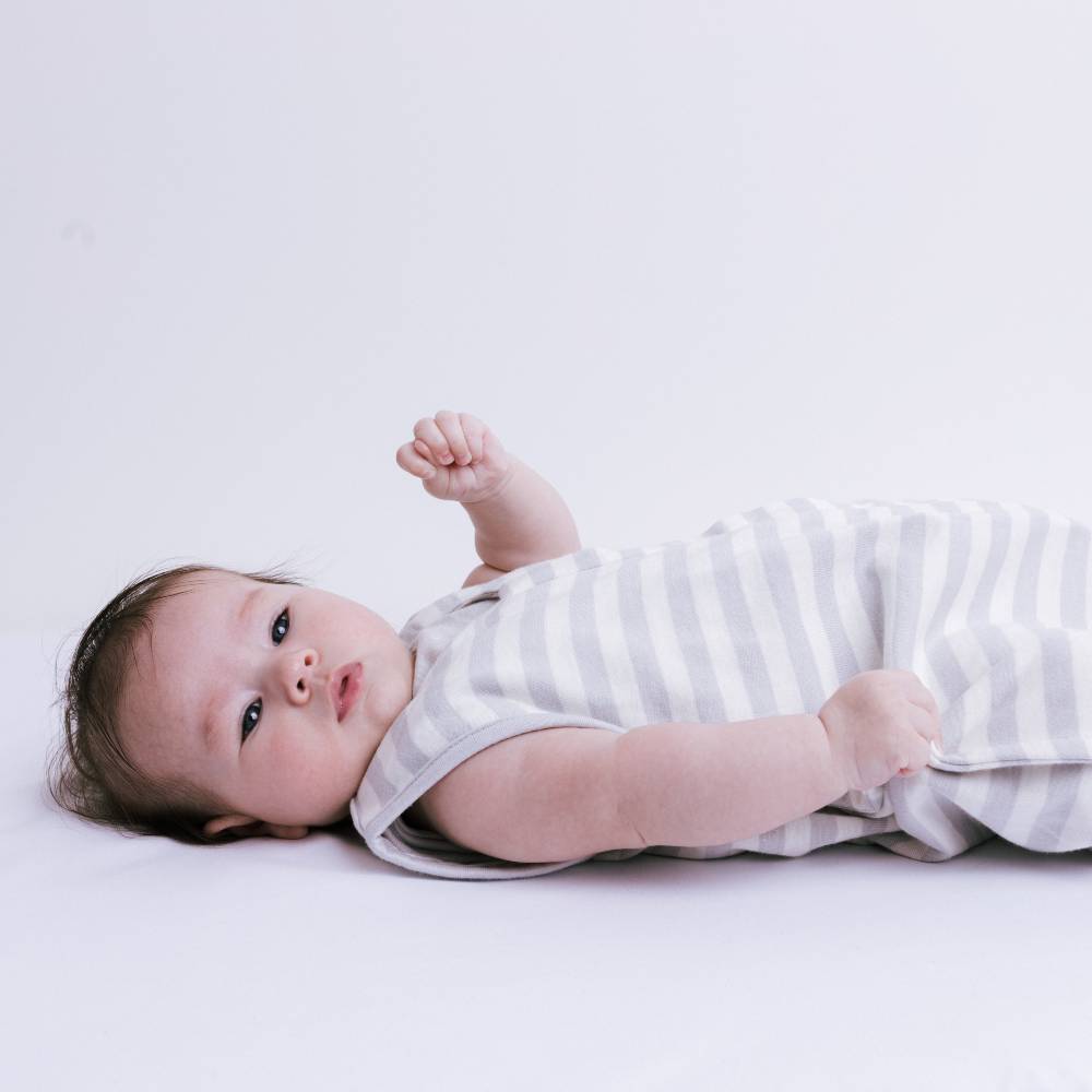 Baby lying on a white surface wearing a striped sleep sack
