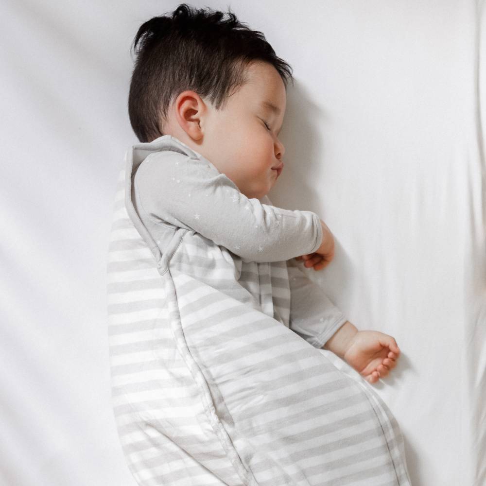 Baby sleeping peacefully in a white crib in  pebble grey sleeping bag