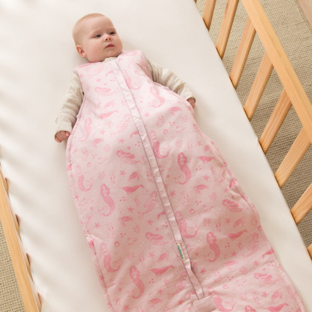 Baby wrapped in a pink sleeping bag with mermaid pattern in a crib