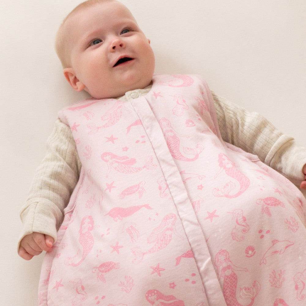 Baby wrapped in a pink mermaid-patterned sleep sack on a white background