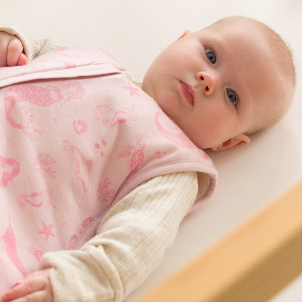 Baby wearing a pink patterned sleeping bag lying on a white surface