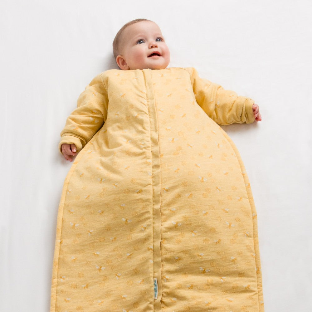 Baby wearing a yellow sleep bag with long sleeves on a white background