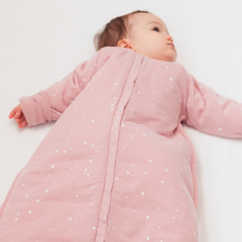 Baby in a pink sleeping bag with star pattern on a white background