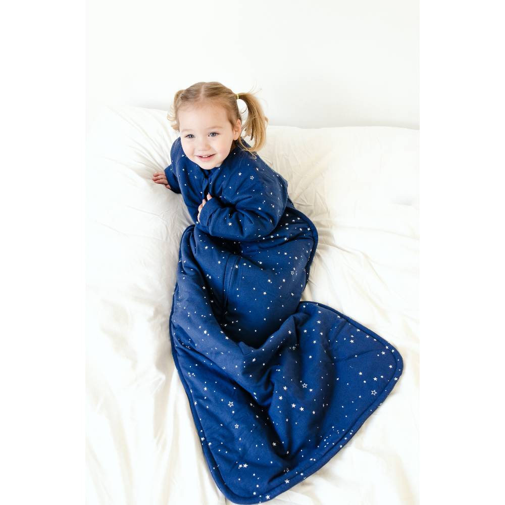 Child cosy in a blue star-patterned sleeping bag on a white bed.
